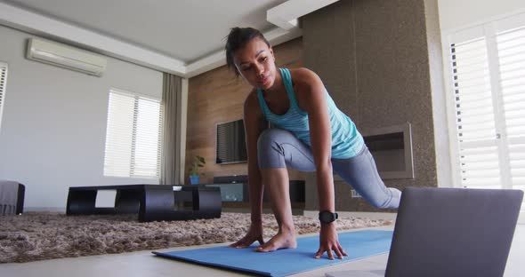 Mixed race woman excercising on a mat with laptop