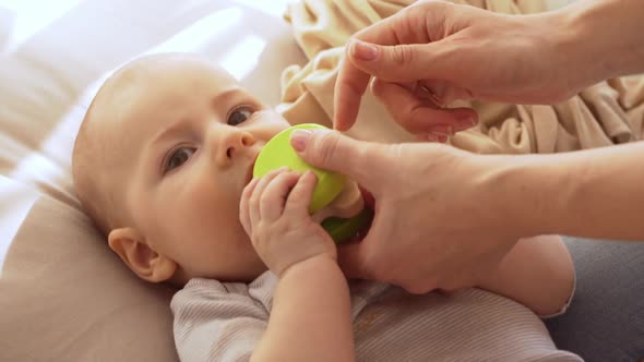 Close Up Footage of Infant Baby Boy Lying on Back and Trying to Eat His Toy While Hand's of Mother