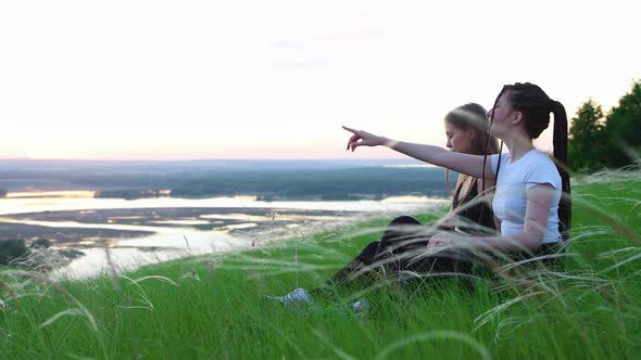 Two Young Women Sitting in the Grass and Watching the Sunset