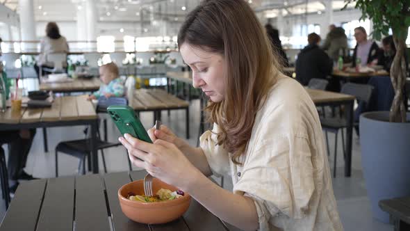 Woman in Cafe Eats Salad Scrolling Social Media Pages