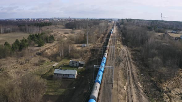 Trasportation scene of industrial train with many tank wagons is passing rural area, leafless trees