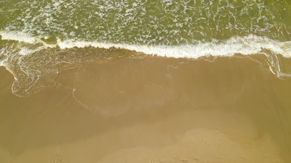 Aerial top down of waves ending at shore and sandy beach of Baltic Sea during sunlight and flying bi