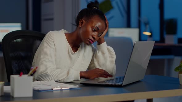 Exhausted African Freelancer Resting Head on Hand in Front of Laptop Working