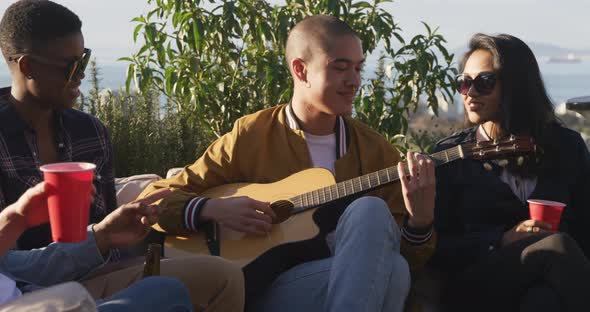 Young man playing guitar on a rooftop with his friends