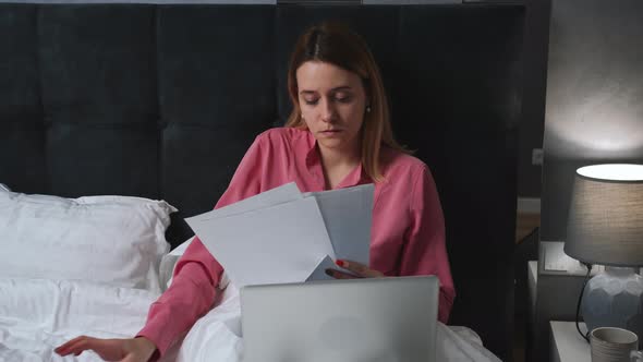 Pretty Caucasian Woman Working with Papers Laptop on Bed at Home Woman Doing Homework on Bed with