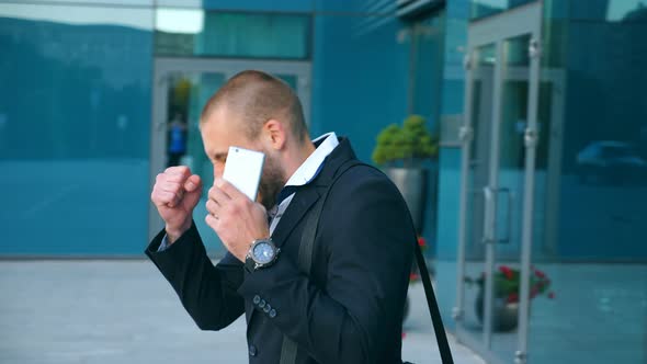 Businessman Talking on Phone Near Office and Celebrating Achievement. Young Business Man Heard Good