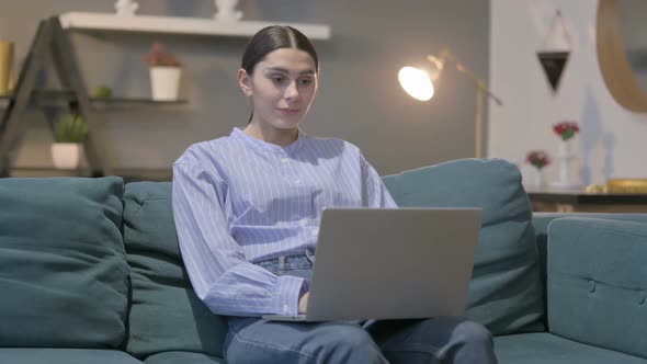 Hispanic Woman with Laptop Celebrating Success on Sofa