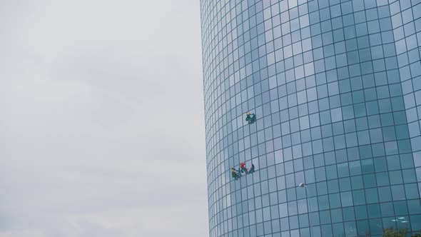 Three Men Workers Hanging on Ropes By the Exterior Blue Windows of a Business Skyscraper -