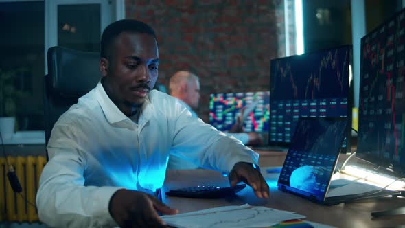 Africanamerican Stockbroker is Using a Calculator While Working