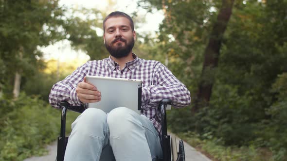 Disabled Man Sitting in Wheelchair in Park Uses Digital Tablet