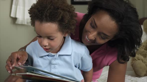 Slow motion of mother cuddling young boy reading book