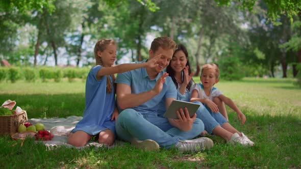 Smiling Family Waving Hands Communicate Using Tablet on Nature in Summer Day