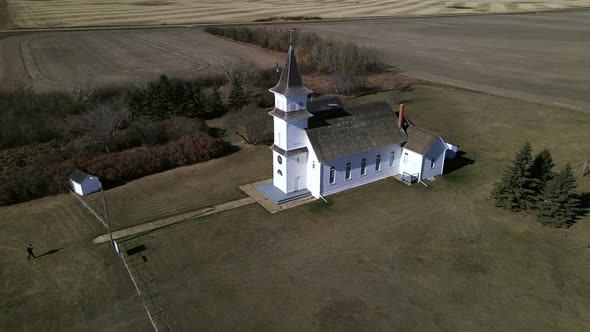 Drone orbiting around old country church in Alberta's prairies while slowly ascending and revealing