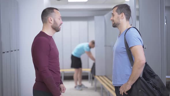 Side View of Two Positive Sportsmen Talking in Locker Room Waiting for Friend Changing Before