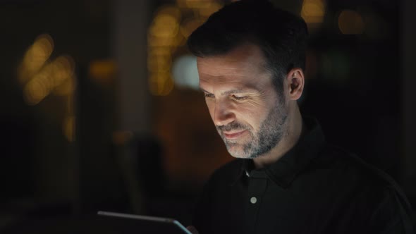 Adult caucasian man using digital tablet at the office in night. Shot with RED helium camera in 8K.