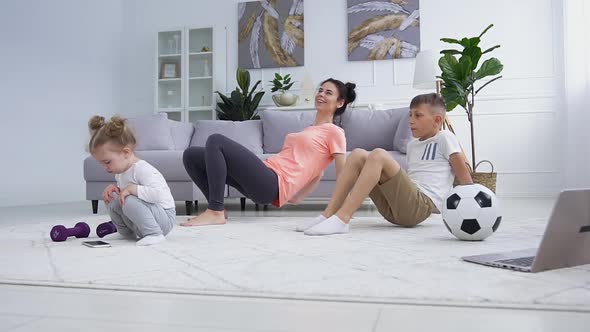 Sportive Mother and Son Doing Sport Exercises while Little Lovely Girl Playing near them