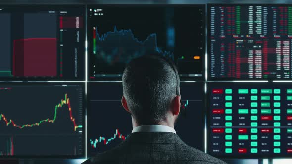 Trader is Working with Multiple Computer Screens Full of Charts and Data Analysis and Stock Broker