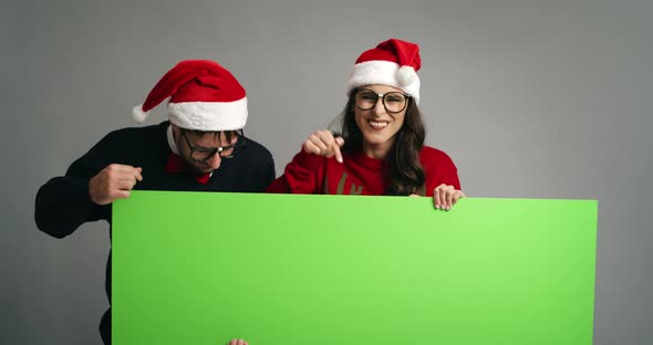 Nerd couple pointing on placard in Christmas clothes