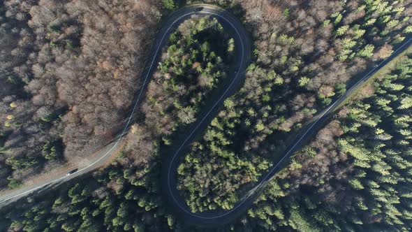 Rising aerial above S shaped road in woodlands of Poland, curved scenic route