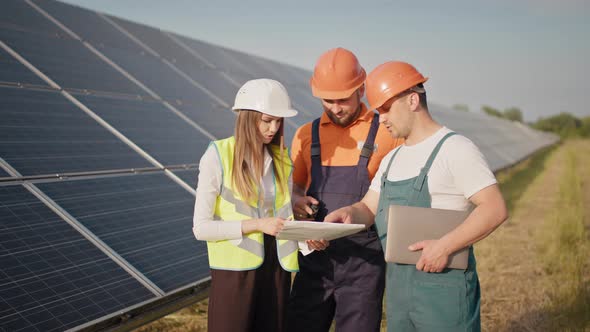 Engineers Use Drawings on the Solar Farm in Special Uniform Standing Look Around