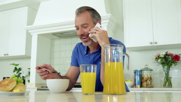 Man talking on mobile phone while having breakfast on dining table