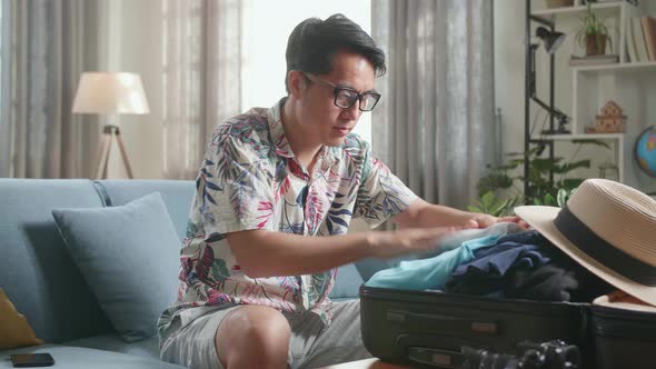 Asian Young Man Packing Clothes In Suitcase At Home, Preparing For Vacation