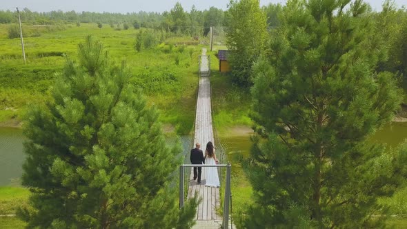 Married Couple Walks on Old Bridge Over River Aerial View