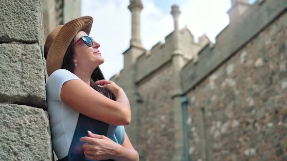 Portrait Smiling Female Tourist in Sunglasses and Hat Admiring Medieval Castle with High Towers