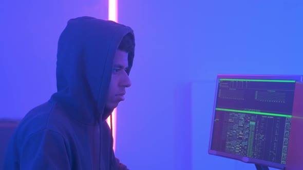 Profile View of African Hacker in Hoodie Working in Room Filled with Display Screens