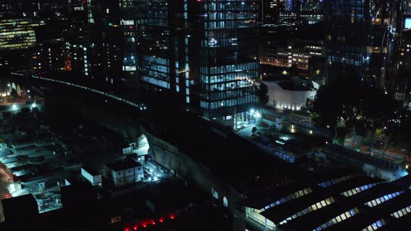 Aerial Night View of Train Arriving Into Station in Between Tall Buildings Modern District