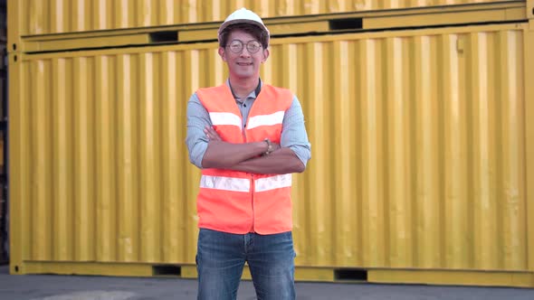 Smiling man in hard hat standing with crossed arms at container cargo site