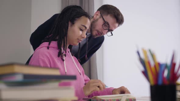 Portrait of Young Caucasian Tutor in Suit and Eyeglasses Helping African American Student with