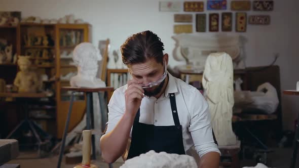 Bearded Male Sculptor Taking off His Glasses Looking at Camera with Nice Smile in His Craft Studio