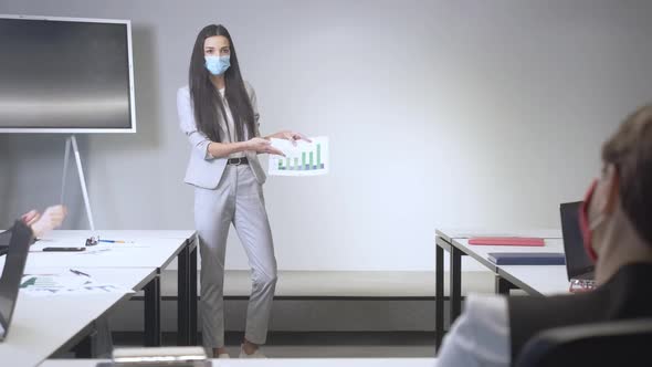 Wide Shot of Confident Young Successful Businesswoman in Covid Face Mask Explaining Graphs in