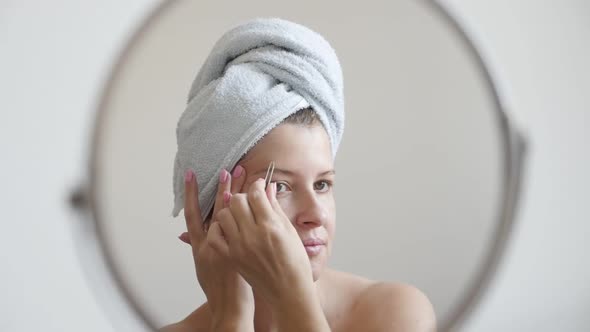 Caucasian woman in front of make-up mirror plucks hair from the face slow-mo  1080p FullHD footage -