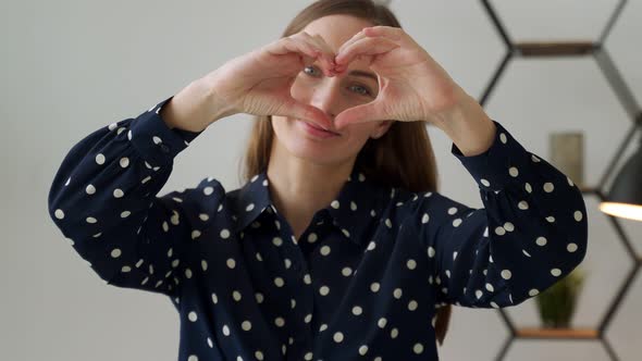 Cute Young Woman Makes a Heart Shape with Her Fingers at Head Level