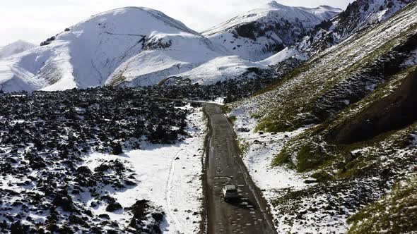 Aerial of Car Driving on Dirt Road Along the Snow Covered Mountains in Iceland