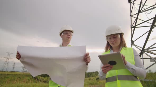 An Electrician Male and Female in the Fields Near the Power Transmission Line