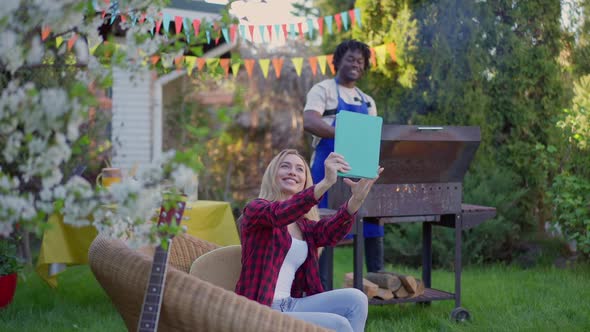 Gorgeous Blond Young Caucasian Woman Boasting African American Man Cooking on Barbecue Grill in