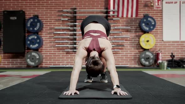 Young Woman in Sportswear Stretching in Downward Dog Position at the Gym