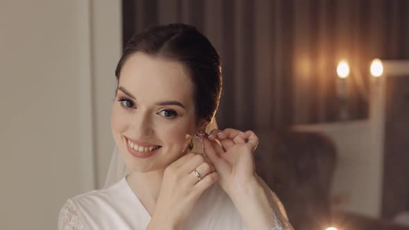 Bride in Boudoir Dress Puts on Earrings Wedding Morning Preparations Woman in Night Gown and Veil