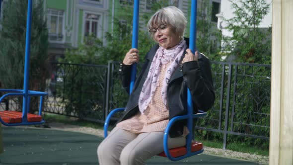 Portrait of Happy Senior Woman Swinging on Swings in Sunshine Outdoors Smiling