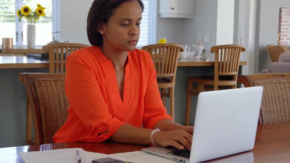 Front view of mixed race mature woman working on laptop on desk at home 4k