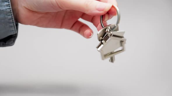 Close-up of a woman's hand in shirt shakes new keys with a metal keychain house.