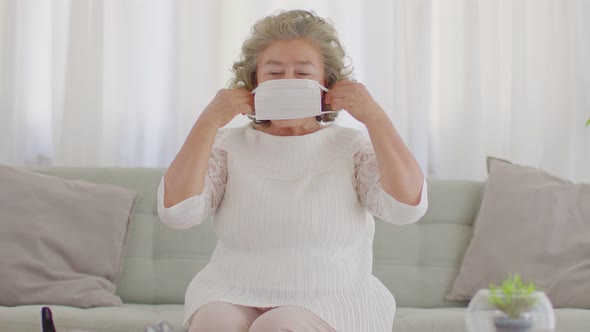 Asian Elderly or Seniors woman wearing medical mask to prevent coronavirus sitting on sofa