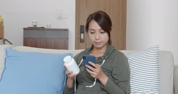 Woman check the ingredients of the bottle of medicine with mobile phone at home