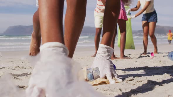 African american parents with two children wearing face masks collecting rubbish from the beach