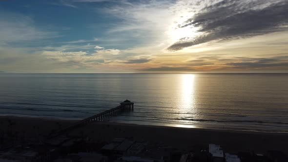 Aerial view over Manhattan Beach Pier, California, with waves crashing on the sandy shoreline, at su