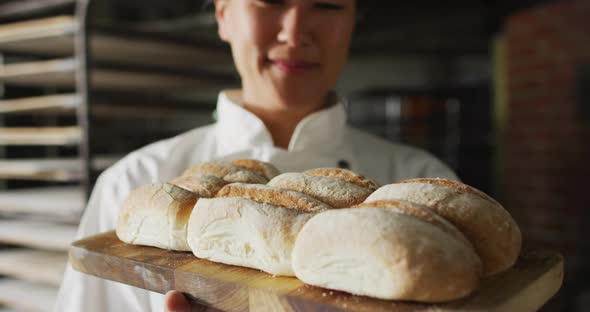 Animation of happy asian female baker holding board with fresh baked bread