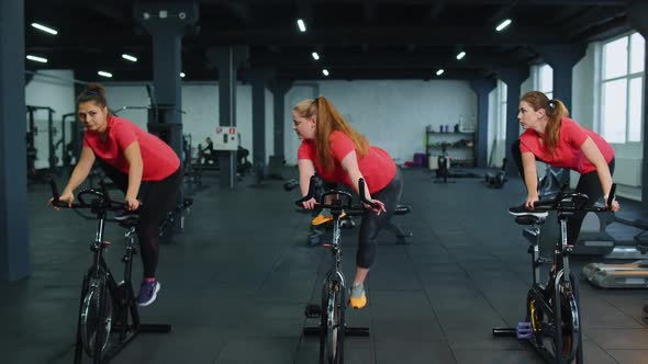 Group Athletic Girls Performing Aerobic Riding Training Exercises on Cycling Stationary Bike in Gym